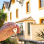 A-man’s-hand-holds-the-keys-to-the-apartment-against-the-background-of-the-house-and-palm-trees.