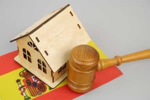 Law and real estate business in Spain. Judge gavel with wooden house model and Spanish flag on gray background.
