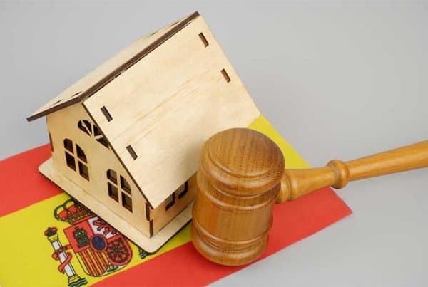 Law and real estate business in Spain. Judge gavel with wooden house model and Spanish flag on gray background.