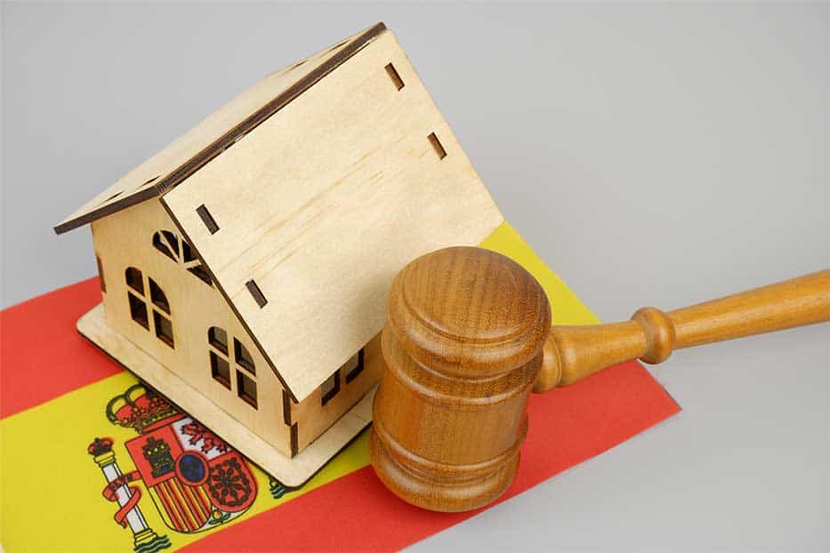 Law and real estate business in Spain. Judge gavel with wooden house model and Spanish flag on gray background.