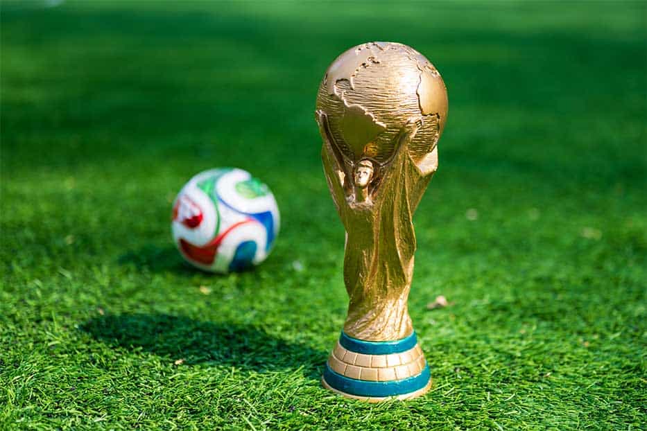 The trophy of the 2026 FIFA World Cup and the official Adidas Trionda ball on the green lawn of the stadium.